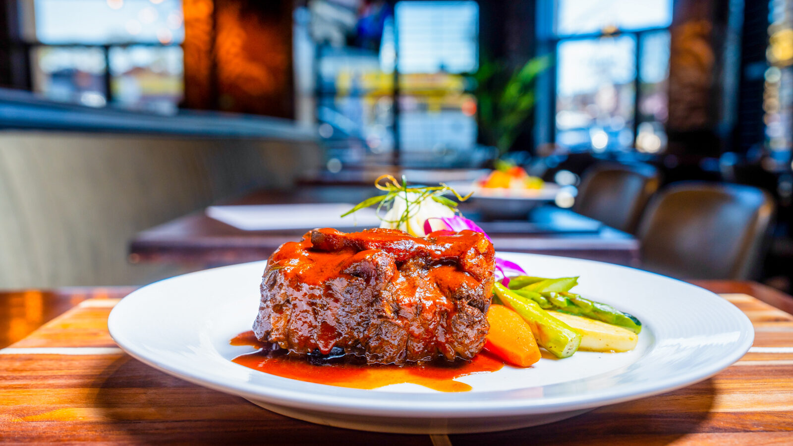 A braised entree plated in the dining room at Bamboo Walk Caribbean Restaurant, with the room soft in the background